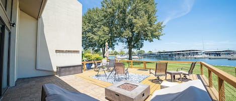A covered outdoor seating area with a fire pit, chairs, and a view of a marina.