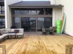 A covered patio with a wooden deck, a sofa, a table, chairs, and a surfboard leaning against the wall. - Lake Conroe, waterfront, boat dock, pets welcome (Montgomery)