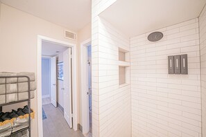 Une salle de bain avec des carreaux de céramique blancs rectangulaires, une douche dotée d’un drain circulaire et un porte-serviettes avec des serviettes pliées.