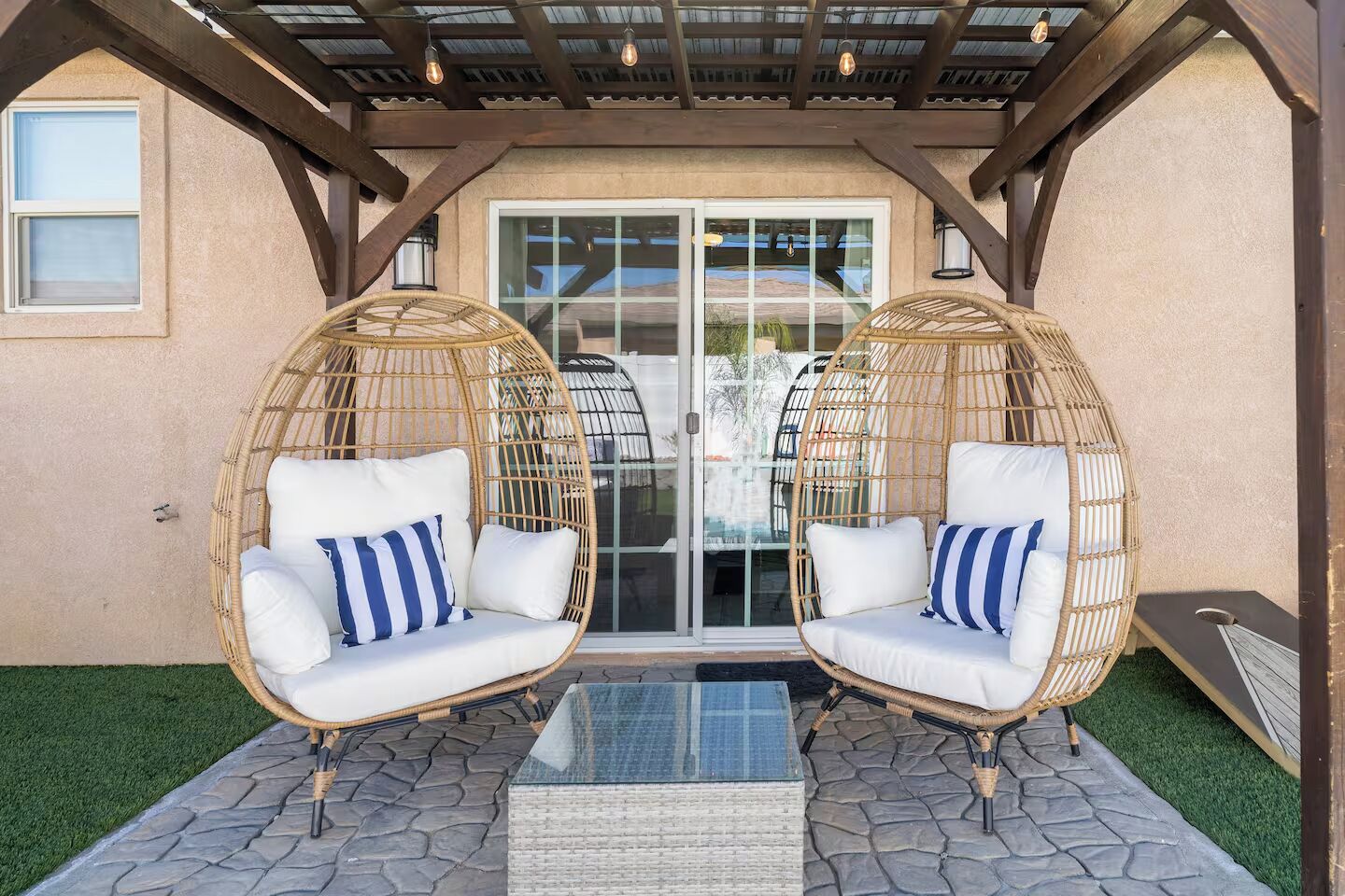 A covered patio with two wicker chairs and a glass table.