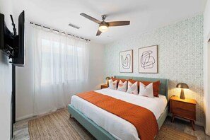 A bedroom with a bed, a ceiling fan, a TV, a nightstand, and two wall art pieces. - Golden Hour - Pool, Spa, BBQ, Mini-Golf, Gameroom! (Indio)