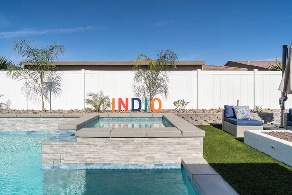 A swimming pool with a white fence, outdoor seating, and a sign spelling 'INDIO'. - Golden Hour - Pool, Spa, BBQ, Mini-Golf, Gameroom! (Indio)