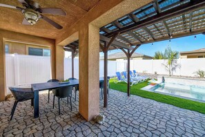 An outdoor patio with a stone floor, a covered seating area, and a pool with lounge chairs. - Golden Hour - Pool, Spa, BBQ, Mini-Golf, Gameroom! (Indio)