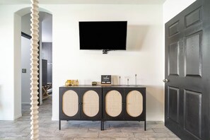 A modern interior with a black console table, a mounted television, and a dark wooden door. - Golden Hour - Pool, Spa, BBQ, Mini-Golf, Gameroom! (Indio)