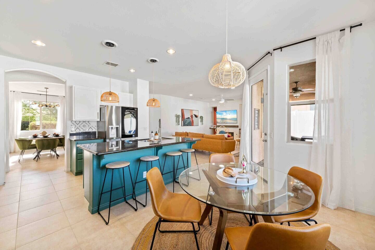 A modern kitchen with a central island, bar stools, a glass dining table, and pendant lighting.