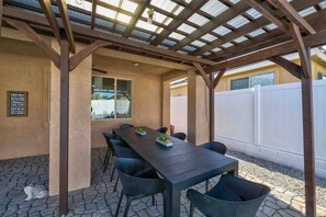 An outdoor patio with a pergola, a table with chairs, and a white fence in the background. - Golden Hour - Pool, Spa, BBQ, Mini-Golf, Gameroom! (Indio)