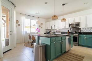 A modern kitchen with white cabinets, a central island, stainless steel appliances, and pendant lighting. - Golden Hour - Pool, Spa, BBQ, Mini-Golf, Gameroom! (Indio)