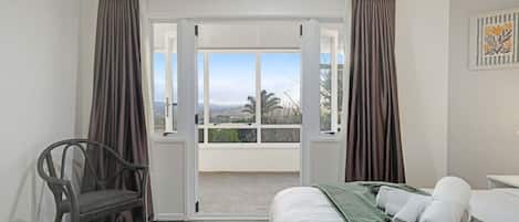 A hotel room with a bed, a chair, a view through a glass door, and a painting on the wall.