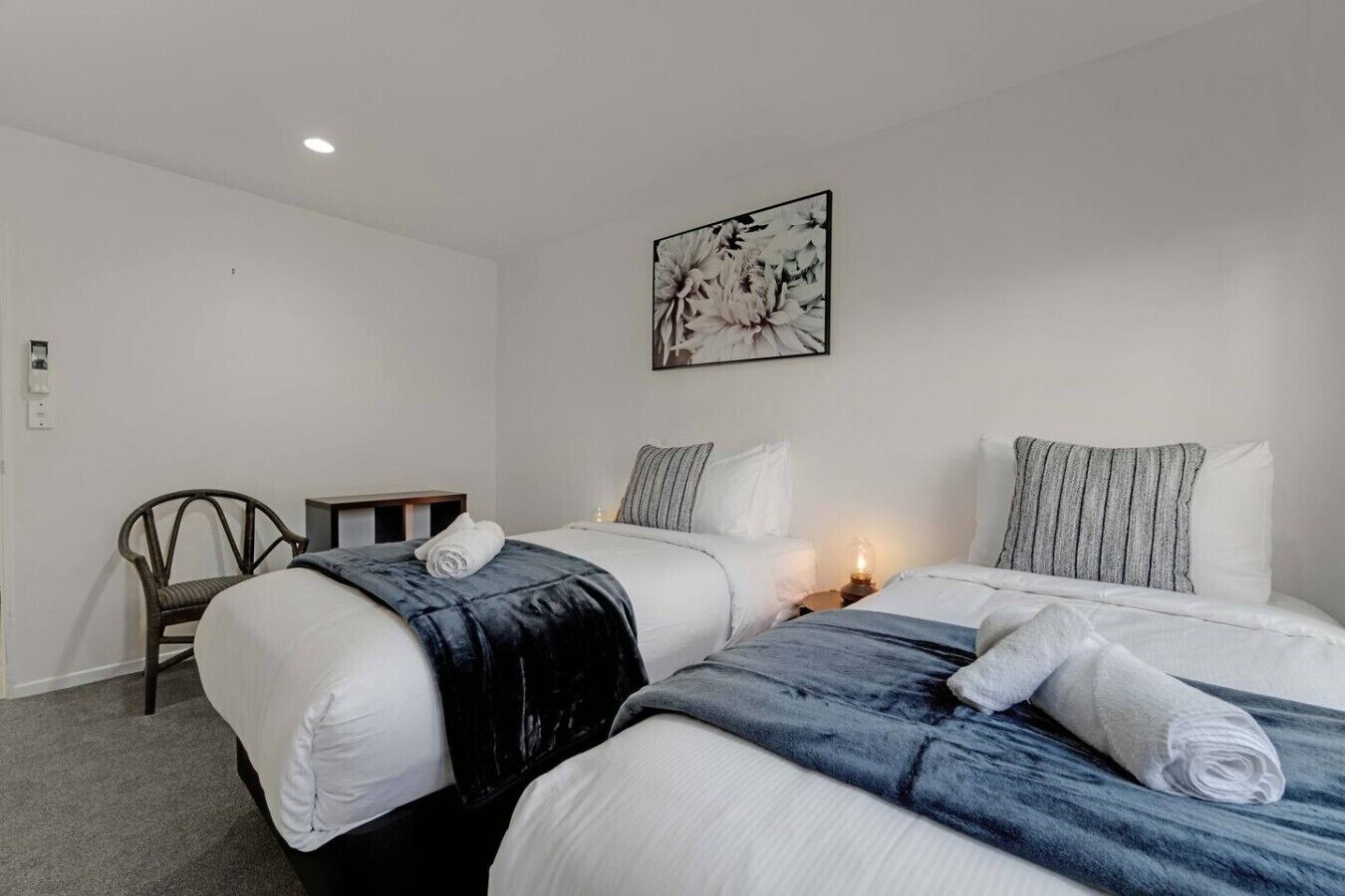 A hotel room with two beds, a chair, a small table, and a wall-mounted artwork.