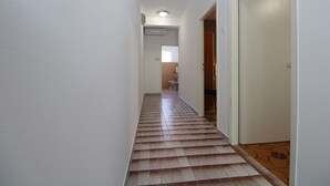 Een smalle gang met betegelde vloer, een deur aan de rechterkant en een badkamer zichtbaar aan het einde.