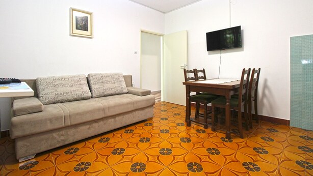 Een woonkamer met een bank, een eettafel met stoelen, een aan de muur bevestigde televisie en een vloer met een patroon.