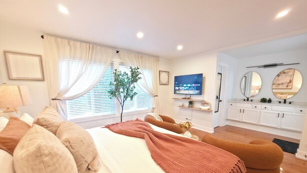 Ett modernt hotellrum med en säng, en tv, en växt och ett badrum med spegel och skåp.