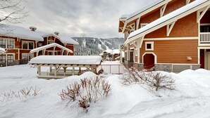 Et snedækket lodge med flere bygninger, en træterrasse og et bjerg i baggrunden.