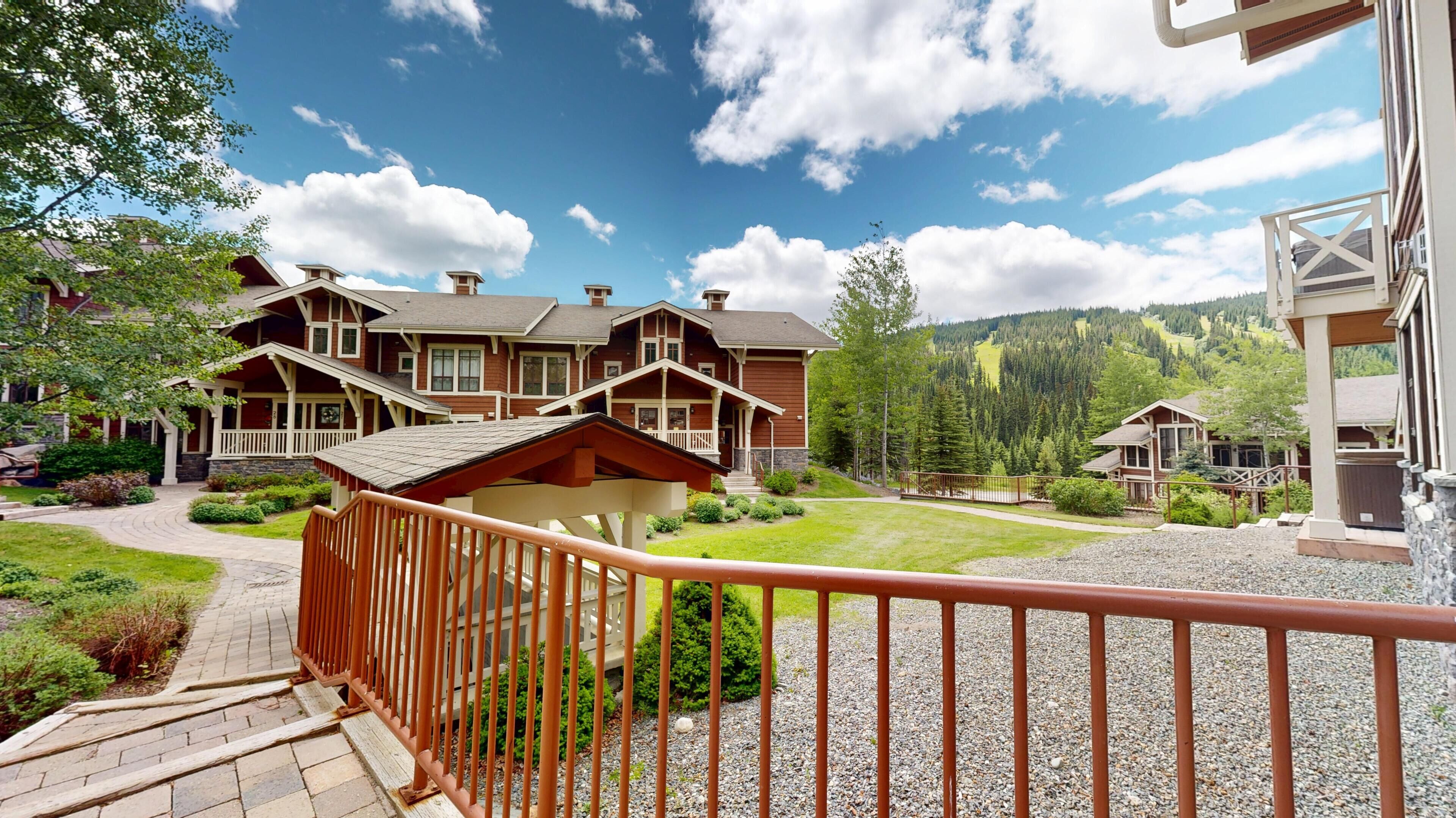 A large lodge with a covered porch, a gravel pathway, and a view of a mountainous landscape.