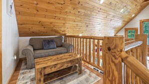 A loft-style room with a wooden ceiling, a sofa, a wooden coffee table, and a view through a window.