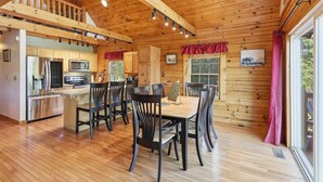 A wooden cabin interior with a dining area, kitchen, and a large window.