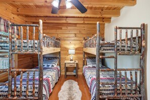 A cabin with four bunk beds, a wooden floor, a fur rug, and a table lamp.