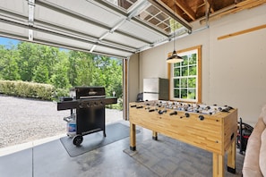 A garage with a barbecue grill, a foosball table, and a refrigerator.