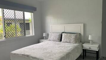 Une chambre à coucher avec un lit, deux tables de chevet et une fenêtre donnant sur un paysage verdoyant.