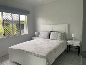 A bedroom with a bed, two bedside tables, and a window with a view of greenery.