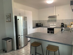 A modern kitchen with white cabinets, stainless steel appliances, a marble backsplash, and two bar stools. - Comfy 4 Bedroom with country views (Atherton)