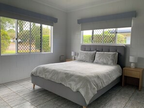 A bedroom with a bed, two bedside tables, and a window with a view of greenery. - Comfy 4 Bedroom with country views (Atherton)