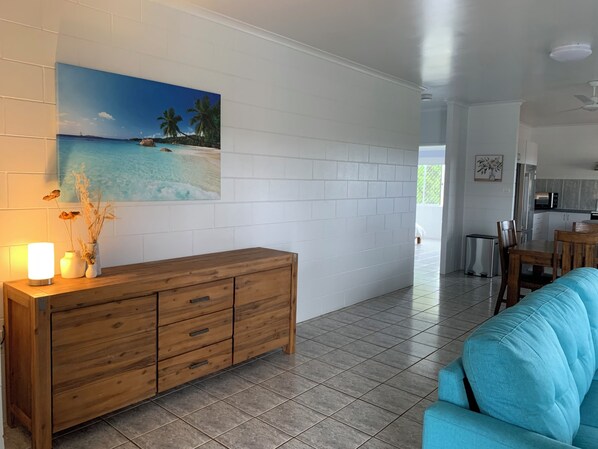 Una sala de estar con un aparador de madera, un sofá azul, un cuadro de una escena de playa y un comedor con mesa y sillas.