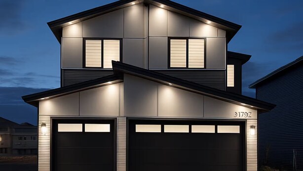 Una casa moderna de dos pisos con garaje, iluminación exterior y cielo despejado.