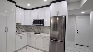 Una cocina moderna con armarios blancos, un refrigerador de acero inoxidable, un microondas y un salpicadero de mármol.