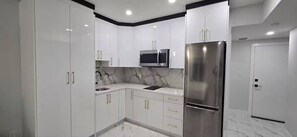 Eine moderne Küche mit weißen Schränken, einem Edelstahlkühlschrank, einer Mikrowelle und einer Marmor-Spritzschutzwand.