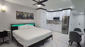 Un dormitorio con cama, escritorio, silla, ventilador de techo y un cuadro en la pared.