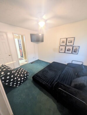 A room with a bed, a bean bag, a flat-screen TV, and framed pictures on the wall.