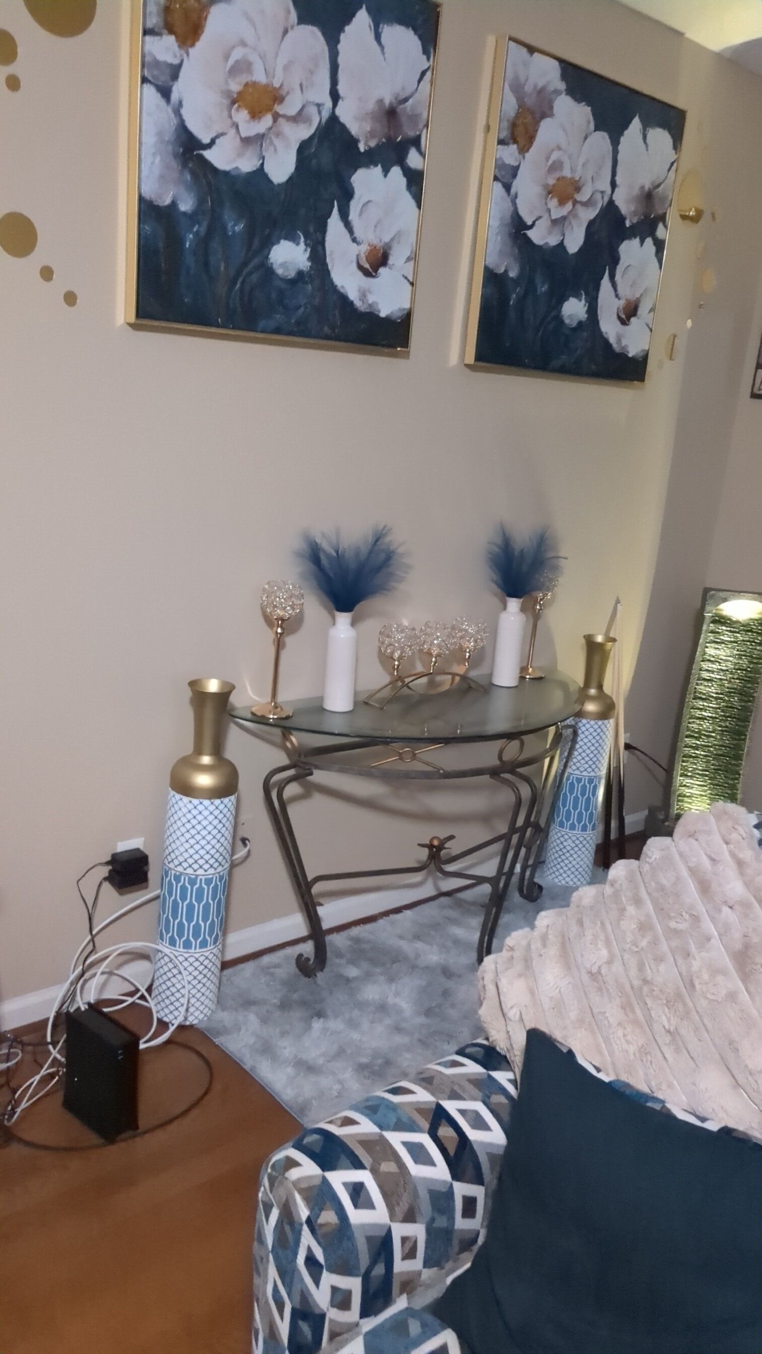 A room with a glass-top table, decorative vases, and a patterned ottoman.