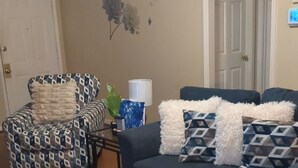 Una sala de estar con un sillón estampado, un sofá oscuro con cojines decorados y una alfombra azul y blanca.