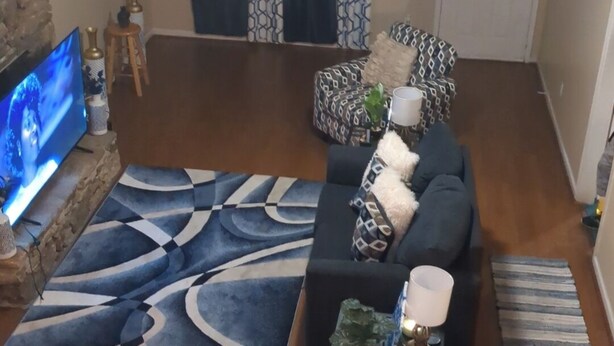 Una sala de estar con un conjunto de sofás, un televisor, un tapete estampado y un ventilador de techo.