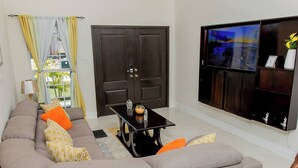 A living room with a sectional sofa, a coffee table, a TV, and a door. - Beyond Escape-2br-gated-15 Min to Ocho Rios (Boscobel)