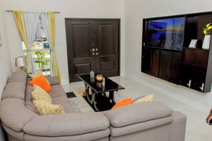 Ein Wohnzimmer mit Ecksofa, Couchtisch, Fernseher und einer Tür.