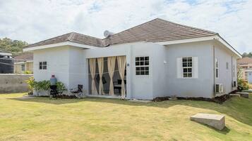 A two-story house with a flat roof, a front porch with a chair, and a small garden area.