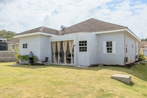 A two-story house with a flat roof, a front porch with a chair, and a small garden area. - Beyond Escape-2br-gated-15 Min to Ocho Rios (Boscobel)