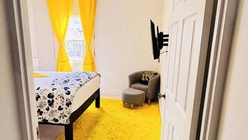 A room with a bed, a chair, a small table, and a ceiling fan.