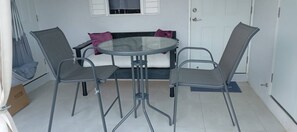 A room with a round glass table, two chairs, a sofa with cushions, and a door. - Beyond Escape-2br-gated-15 Min to Ocho Rios (Boscobel)