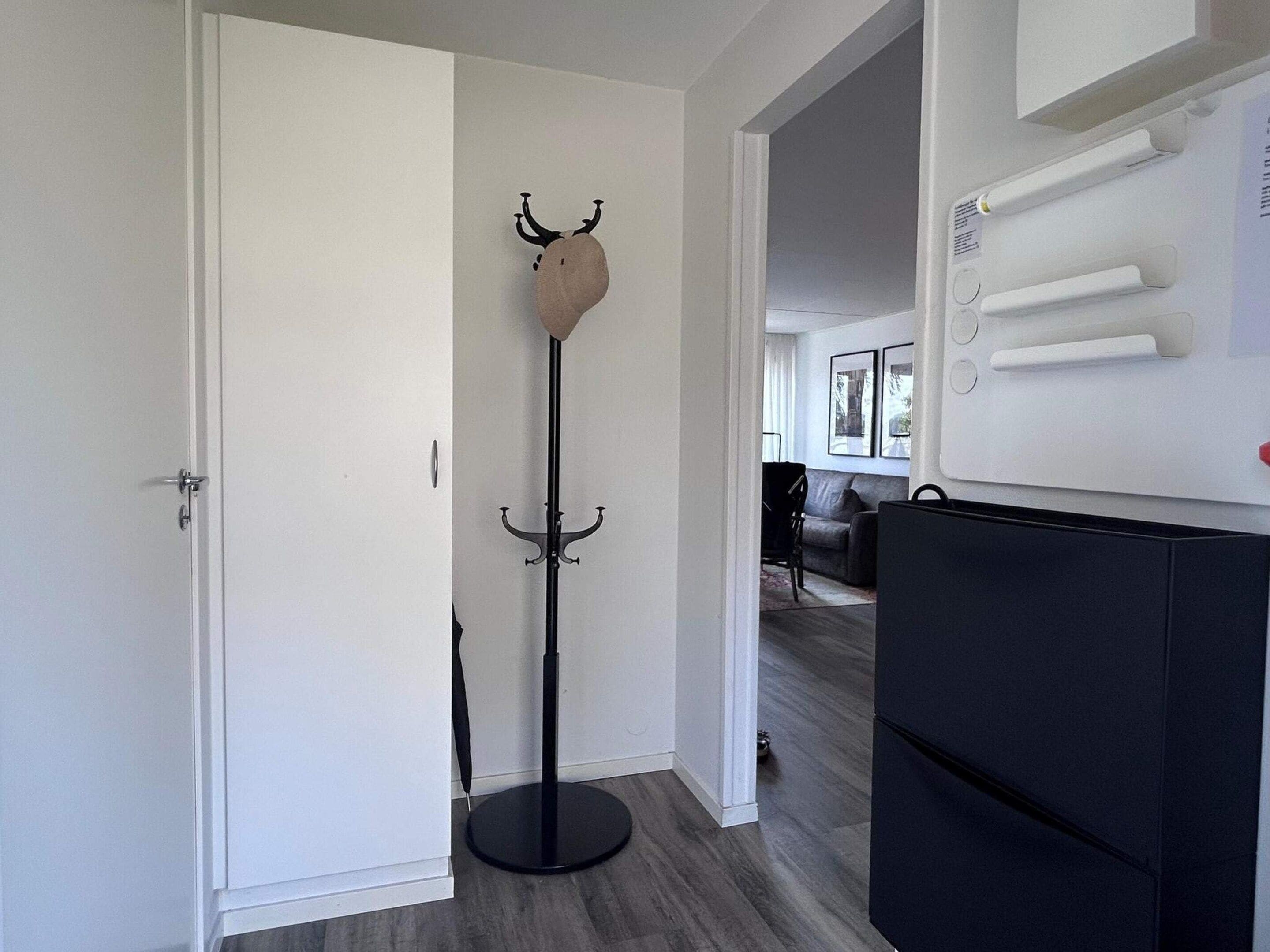 Corredor com um cabideiro, uma porta e um eletrodoméstico preto, possivelmente uma geladeira.