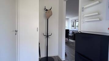 Corredor com um cabideiro, uma porta e um eletrodoméstico preto, possivelmente uma geladeira.