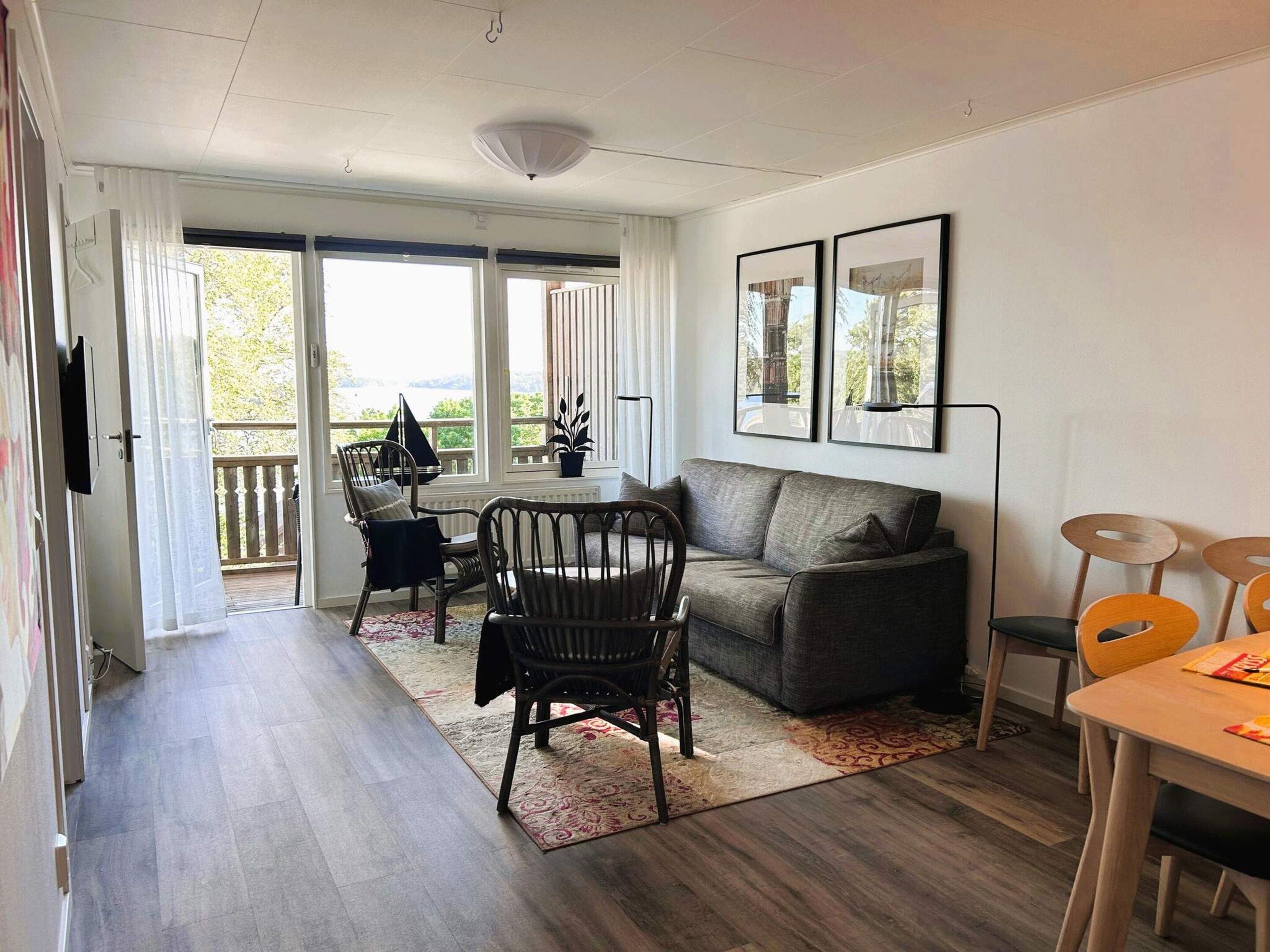 Una sala de estar moderna con un sofá, sillas, una mesa de comedor y un balcón con vistas.