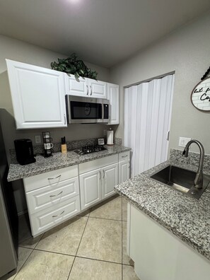 A kitchen with white cabinets, a microwave, a coffee maker, a sink, and a decorative wall piece. - Cozy & Modern Studio near Strip, Freemont & LVCC. Free Parking & Private Patio. (Las Vegas)