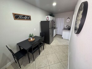 A compact kitchen with a refrigerator, a dining table with chairs, a potted plant, and a wall-mounted sign. - Cozy & Modern Studio near Strip, Freemont & LVCC. Free Parking & Private Patio. (Las Vegas)