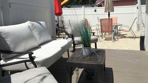 Patiolla on valkoinen ulkokäyttöön tarkoitettu sohva, punottu pöytä ja ruukussa oleva kasvi.