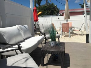 Eine Terrasse mit einem weißen Outdoor-Sofa, einem Korbtisch und einem Blumentopf.