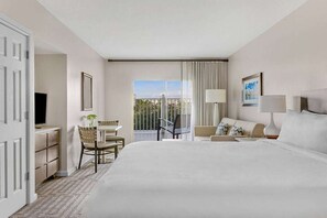 Ein Hotelzimmer mit einem Bett, einem Schreibtisch, einem Sessel, einer Couch, einem Fernseher und einem Fenster mit Vorhängen.