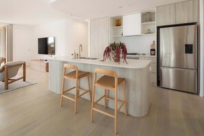 A modern kitchen with a central island, stainless steel appliances, and wooden bar stools. - Mahlo by Khove (Burleigh Heads)